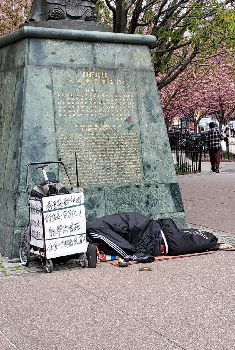 一华人游民睡在曼哈顿唐人街的孔子像前面。（陈家龄提供）